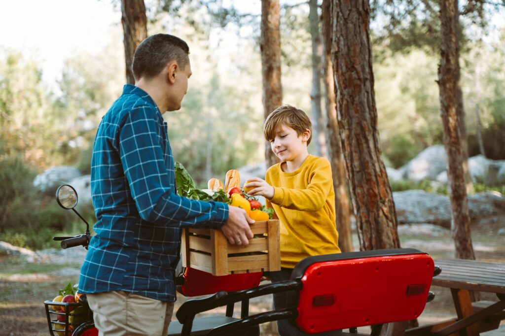 Farmer father and school boy kid delivered wooden crates with vegetables to camp site for picnic