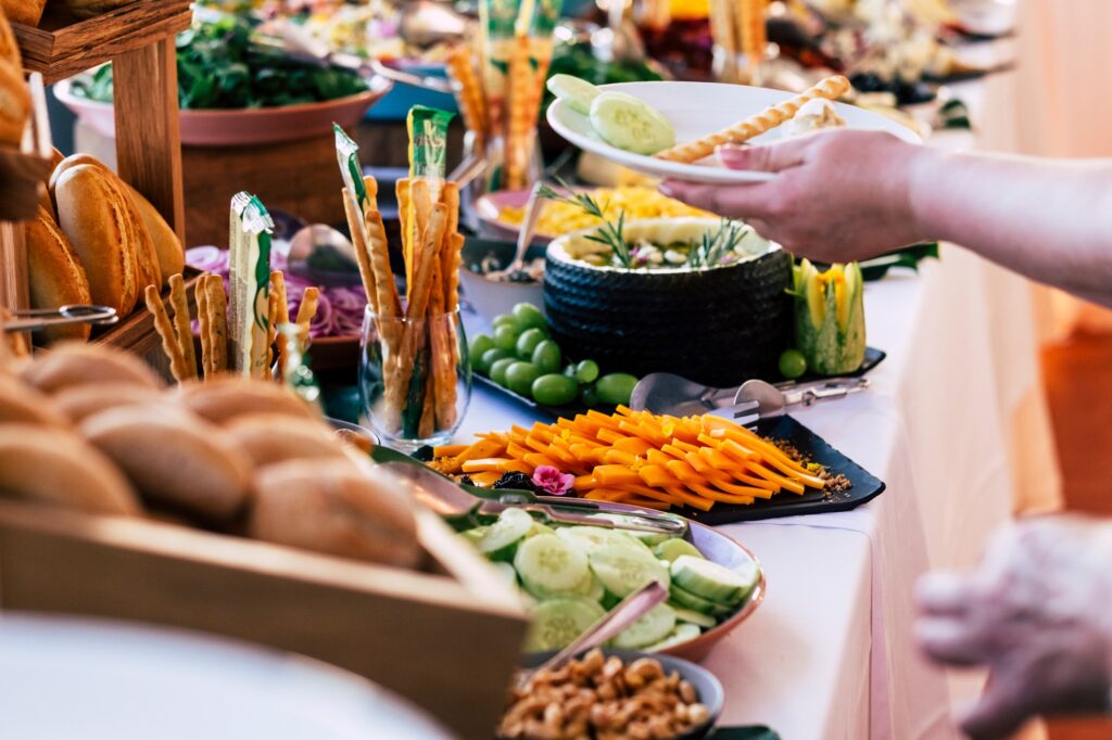 Close up of catering service table full of food and people serving and taking on dishes.